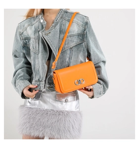 Detail of a bright orange crossbody bag with a metallic silver buckle shown on a model