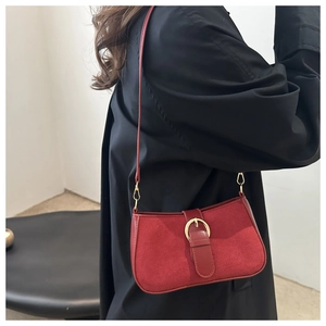 Close-up of red suede underarm bag with gold circular buckle and metal hook detail