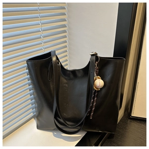 Detail view of black oil wax leather tote bag with creative baseball pendant