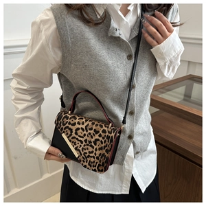 Détail du sac à bandoulière léopard avec accent métallique porté par un mannequin dans un décor chic