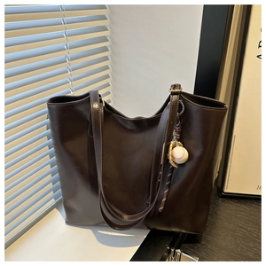 Close-up of deep brown leather tote bag featuring a decorative baseball keychain ornament