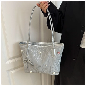 Détail d'un sac cabas argenté avec des perles blanches et un charm nœud en cristal