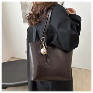 Detail of dark brown tote bag with baseball charm on shoulder strap in lifestyle setting