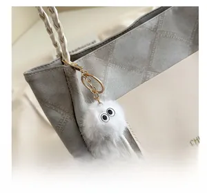 Close-up of white plush monster keychain with large eyes and metal clip on tote bag