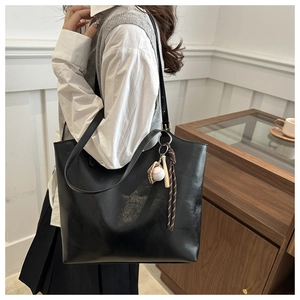 Detail of glossy black faux leather tote with creative baseball glove bag pendant