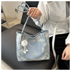 Close-up of blue quilted tote bag with woven shoulder strap and fuzzy monster charm