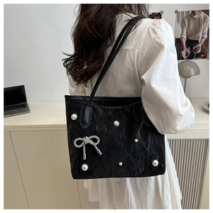 Détail d'un sac cabas noir avec perles blanches, nœud scintillant et texture plissée