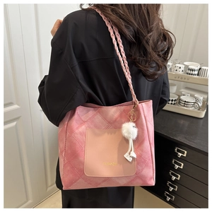 Detail of pink quilted tote bag with braided strap and plush charm worn by model
