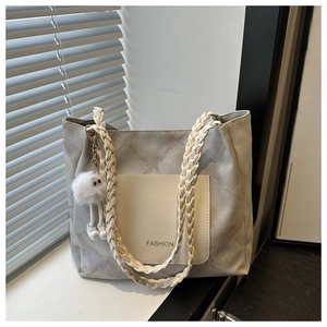 Close-up of quilted grey tote bag with woven strap, front pocket, and plush charm detail