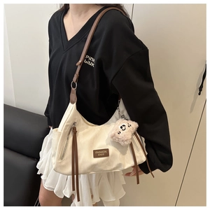 Detail of cream nylon crescent bag with brown trim, tassels and bear charm on model