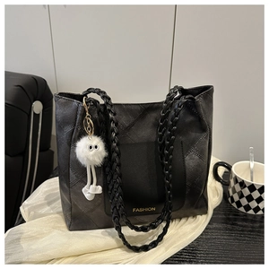 Detail of black quilted tote bag with woven shoulder straps and plush charm accessory