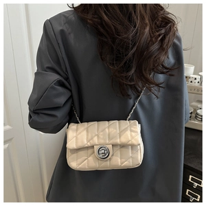 Detail view of a cream quilted crossbody bag with silver chain strap and metal turn-lock
