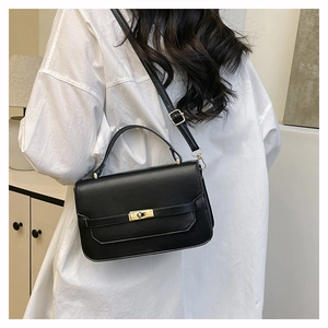 Sac à bandoulière noir avec boucle dorée porté sur une chemise blanche oversize