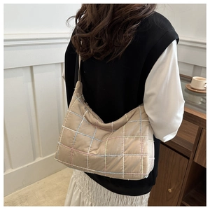 Detail of light beige quilted tote bag with colorful stitching shown on a shoulder