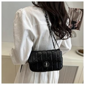 Detail view of quilted black leather chain bag with silver clasp on white dress model