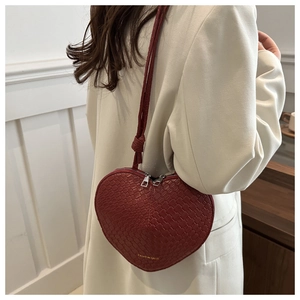 Close-up of heart-shaped woven burgundy crossbody bag with silver zipper and leather strap