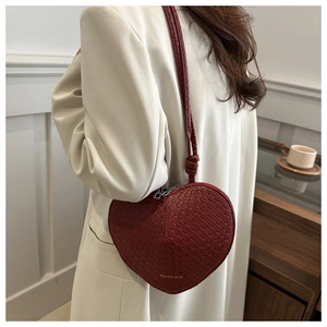 Side view of a red heart-shaped crossbody bag with woven texture on a model