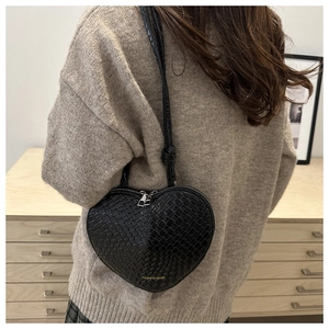 Close-up of black heart-shaped woven bag worn by a model in a cozy indoor setting