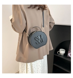Detail of black round crossbody bag featuring embossed SM logo and matte leather texture
