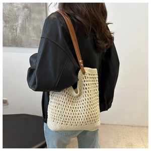 Detail of off-white crochet bucket bag with brown leather strap worn by a model