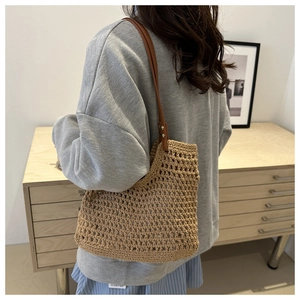 Detail of hand-woven hollow bucket bag with brown leather strap and metal rivets