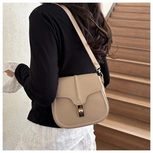Elegante borsa a sella beige con chiusura dorata indossata a spalla in un set di classe