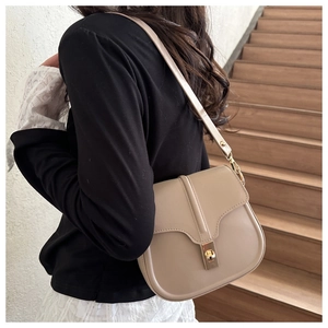 Beige saddle bag with gold buckle shown on shoulder of model in a home setting