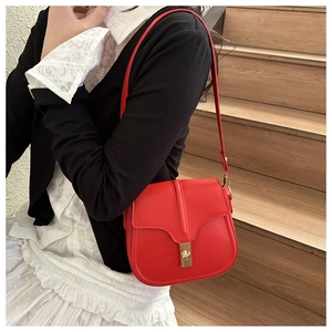 Model wearing a red saddle bag with a gold twist lock on an adjustable strap