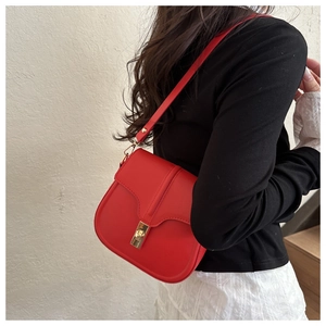 Detail view of a bright red crossbody bag with gold metal clasp on a model's outfit