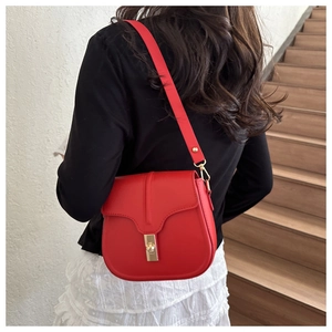 Detail of red saddle bag featuring a gold twist lock clasp and adjustable leather strap
