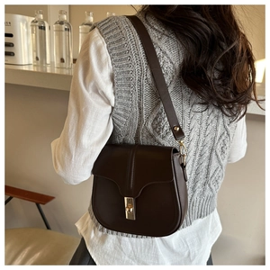 Detail of a brown vintage leather saddle bag with gold hardware worn by a model