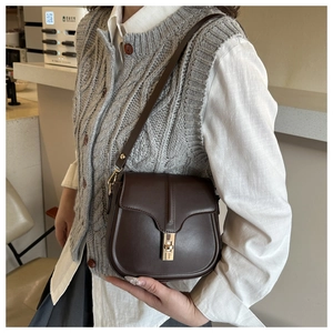 Detail of a dark brown leather saddle bag with gold metal lock and adjustable strap
