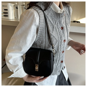Detail of a black leather saddle bag with gold buckle worn by a model in casual attire