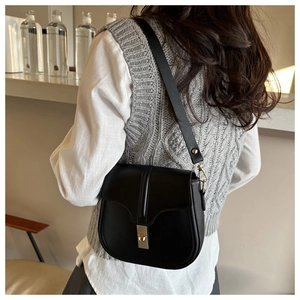 Borsa a sella in pelle nera opaca con fibbia dorata indossata su un gilet grigio