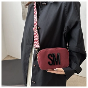 Close-up of burgundy square bag with SM logo and geometric pattern wide strap