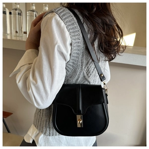 Dettaglio di una borsa a sella in pelle nera opaca con chiusura a scatto dorata e tracolla
