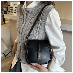 Close-up of black leather saddle bag with gold buckle on a model in a cafe