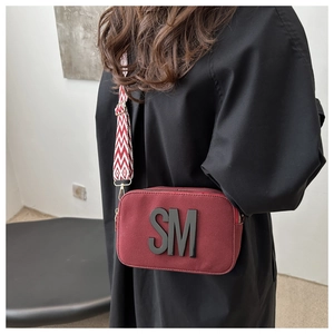 Detail of burgundy crossbody bag featuring black SM lettering and geometric wide strap