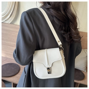 Detail of ivory white saddle bag with golden buckle on a grey blazer-clad model