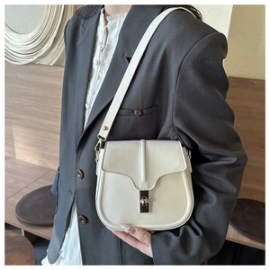 Close-up of ivory leather saddle bag worn with a charcoal grey blazer in a minimalist setting