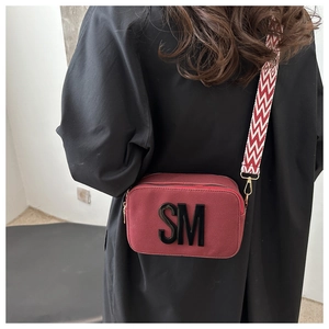 Detail of red crossbody camera bag with bold SM logo and geometric wide shoulder strap