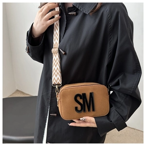 Detail of brown suede crossbody camera bag with bold SM letter and wide woven strap