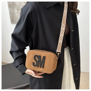 Close-up of brown suede camera bag featuring geometric wide strap and 3D SM letter detail