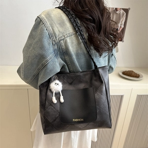 Quilted black tote bag with woven strap and plush charm shown in an aesthetic interior