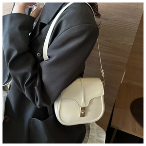 Dettaglio di una borsa a sella bianca in pelle con fibbia dorata su un blazer grigio