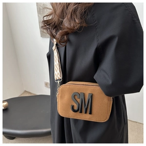 Détail du petit sac carré en daim caramel avec lettres 3D et bandoulière à chevrons