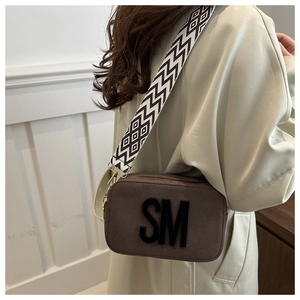 Détail du sac caméra en daim marron foncé avec large bandoulière géométrique et logo