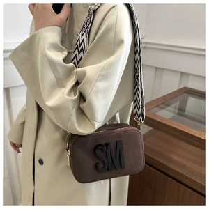 Détail d'un sac caméra en daim marron avec lettres SM et bandoulière large tissée