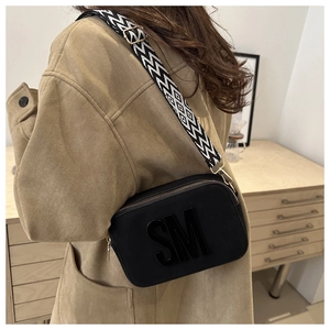 Detail of black crossbody bag featuring a 3D SM logo and geometric wide shoulder strap