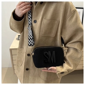 Détail du sac caméra noir avec large bandoulière géométrique et décor de lettre SM